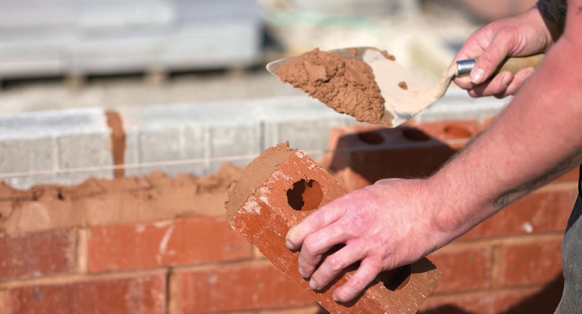 builder laying bricks to create a wall