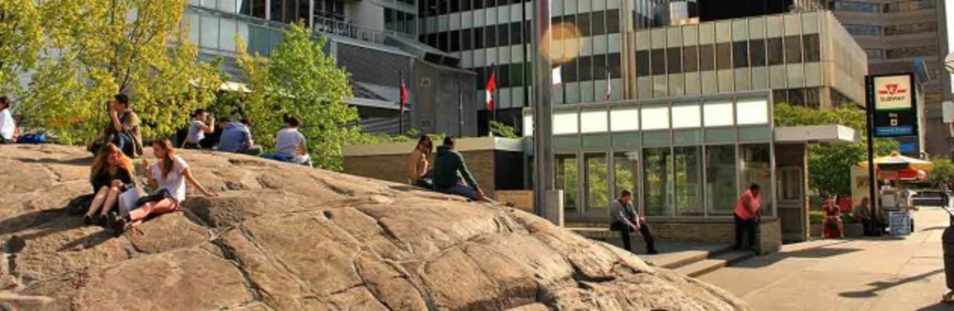 People socialising a top a large rock infront of a modern urban landscape. 
