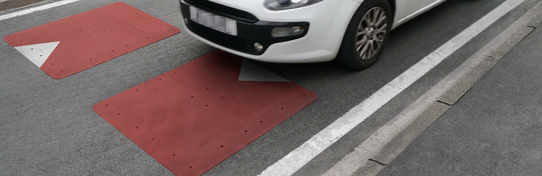 White car driving over a red reinforced speed cushion.