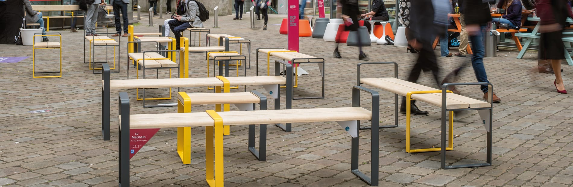 Members of the public sitting on and waling around temporary street furniture benches