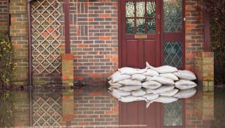 A flood of water in front of a house with sandbags protecting the front door