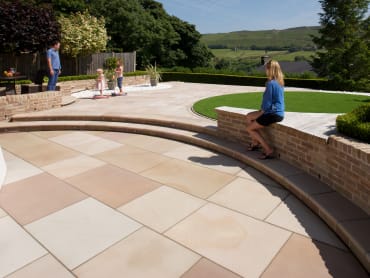 marshalls sawn versuro kingsize in autumn bronze multi set in a garden with steps and a circular grass area with family playing.