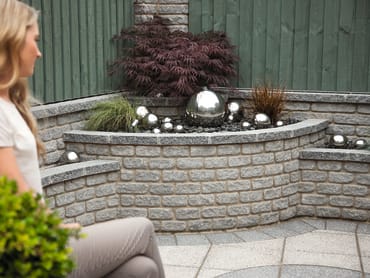 marshallite walling in rustic finish and ash multi colour used as raised bed planter with woman looking at the water feature