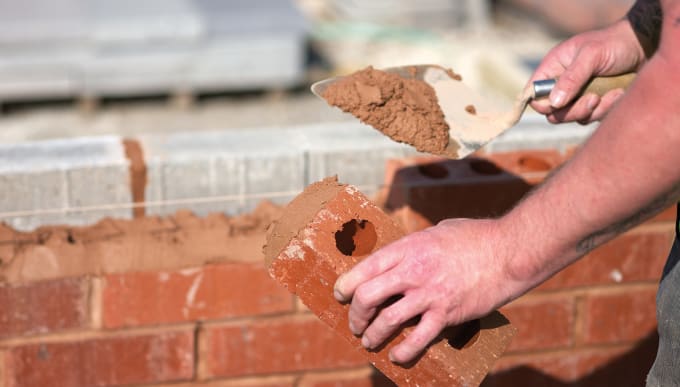 man laying a brick wall with mortar