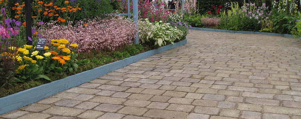 a winding cobbled path is bordered by bright bedding plants to the left of the walkway